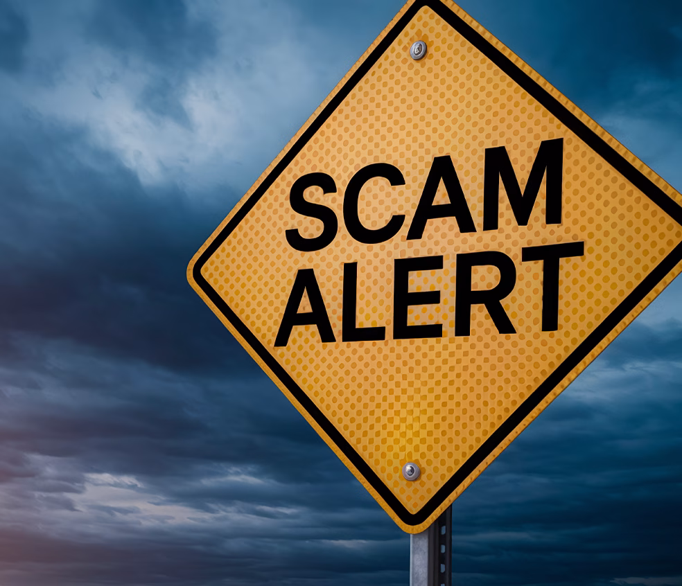 Yellow road sign reading "Scam Alert" against a dark, cloudy sky background, warning of potential fraud or deception.